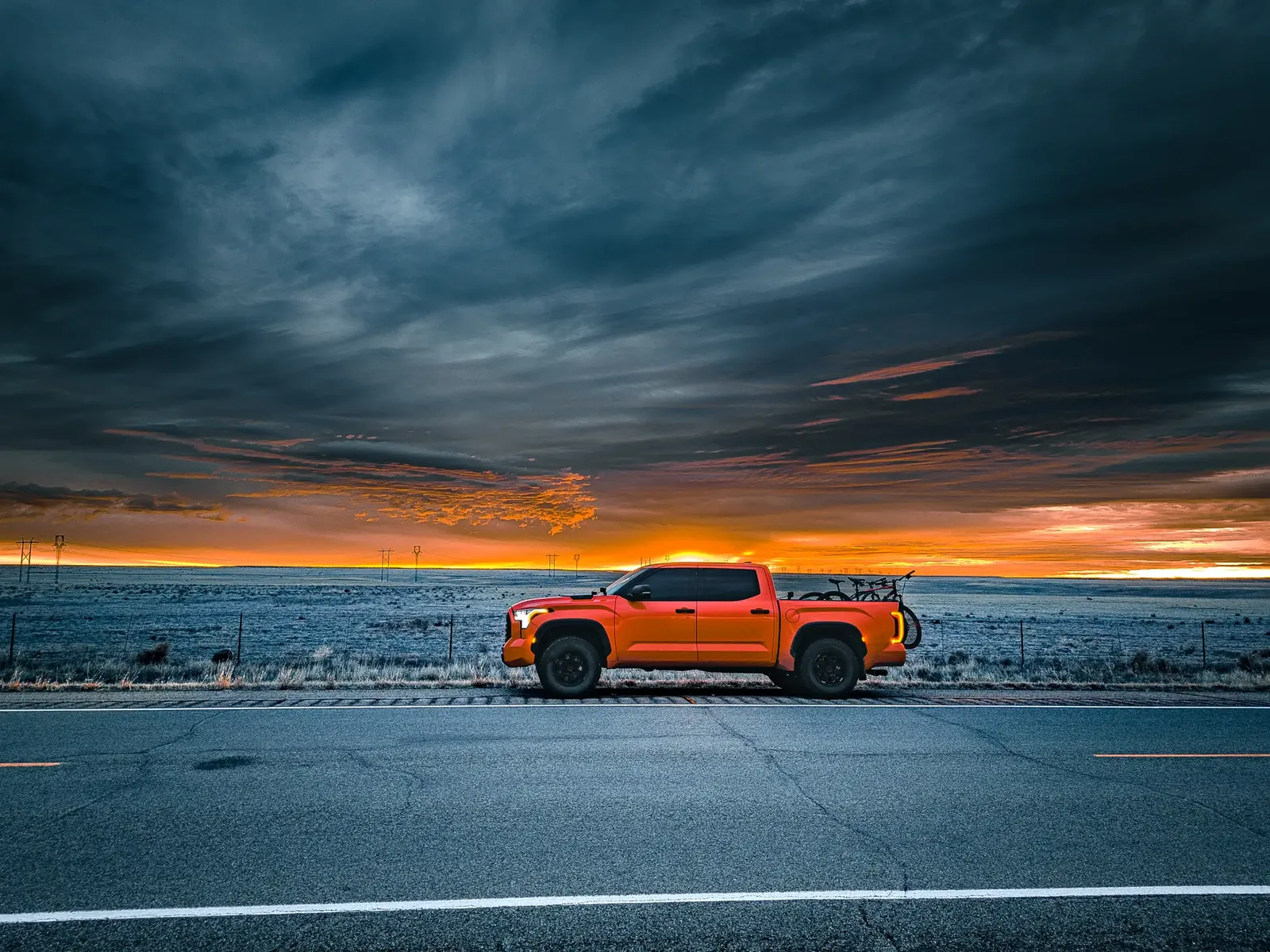 Orange Tundra parked roadside on a straight highway, dramatic sunset sky over flat plains.