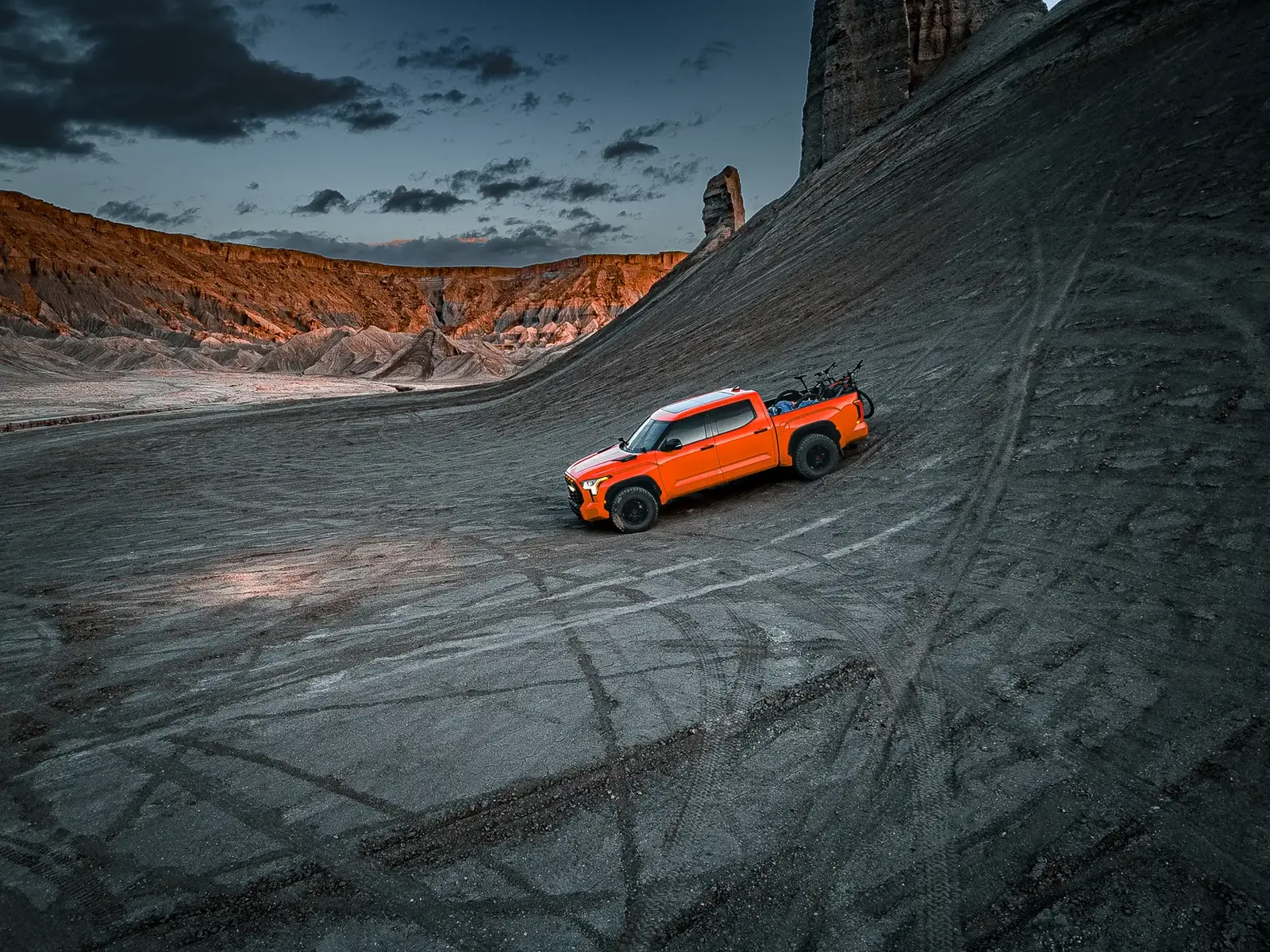 Aerial drone shot of Drew's former orange Tundra on a grey ash slope with tire tracks at dusk, Swing Arm City OHV area (Caineville / Factory Butte, Utah).