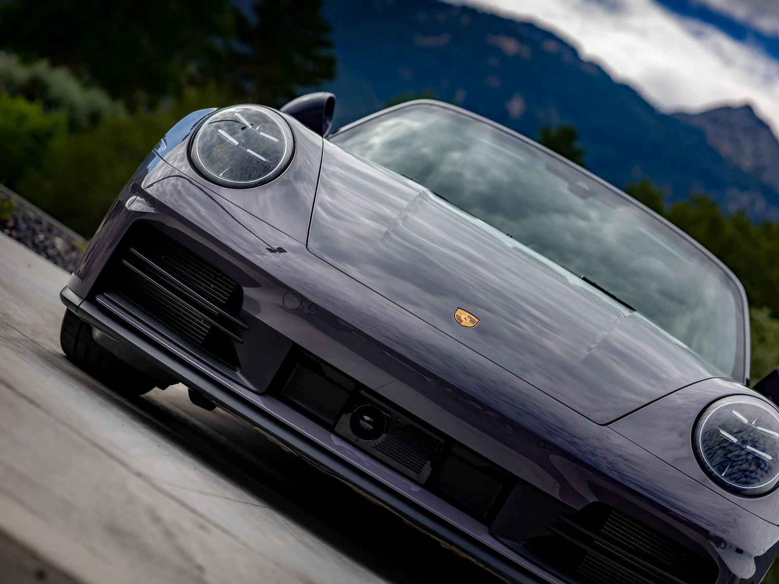 Low-angle Canon EOS R8 photograph of a gray Porsche 911 beneath mountain clouds.
