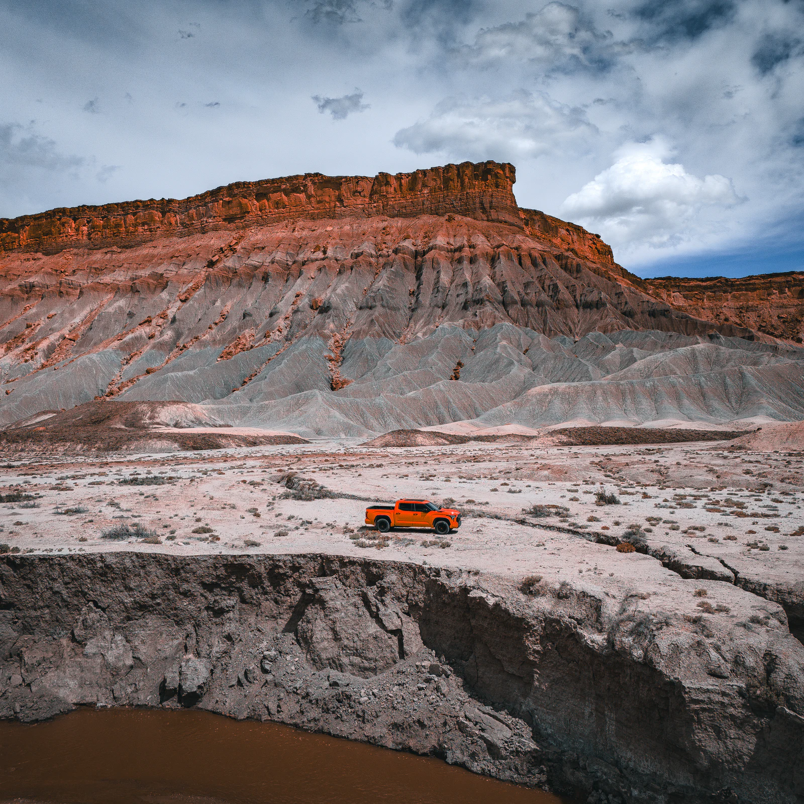 Aerial DJI photograph of Drew's orange Tundra crossing pale badlands beneath a storm sky.
